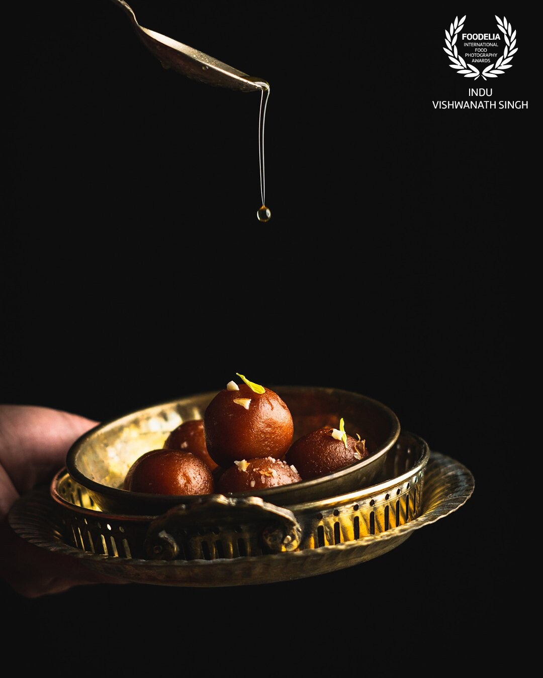 The drip of liquid sugar is the highlight of this image with the hint of Indian culture with the help of antique Indian props. Gulab Jamuns are a traditional festive dessert in India