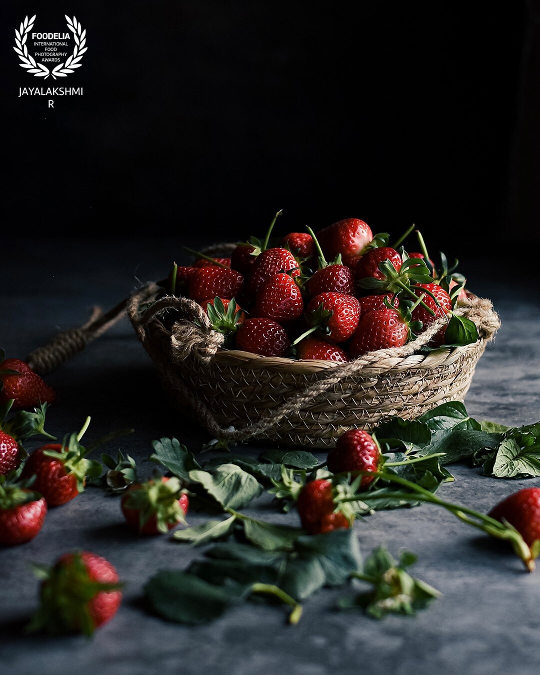 Farm fresh strawberries set up in a dark moody frame . Added leaves to throw in some pop of color . Shot in natural light against a small window .