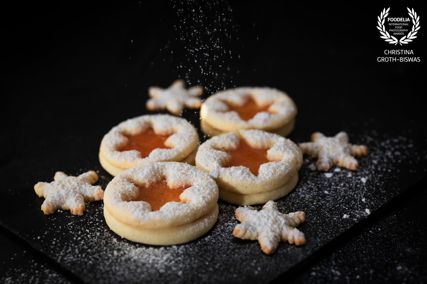 Linzer cookies filled with a homemade apricot and vanilla jam. I like taking my food pictures my own way, without (m)any props. This applies to Christmas cookies as well. The black background brings out the bright orange of the jam and the icing sugar adds a bit wintery touch to it.