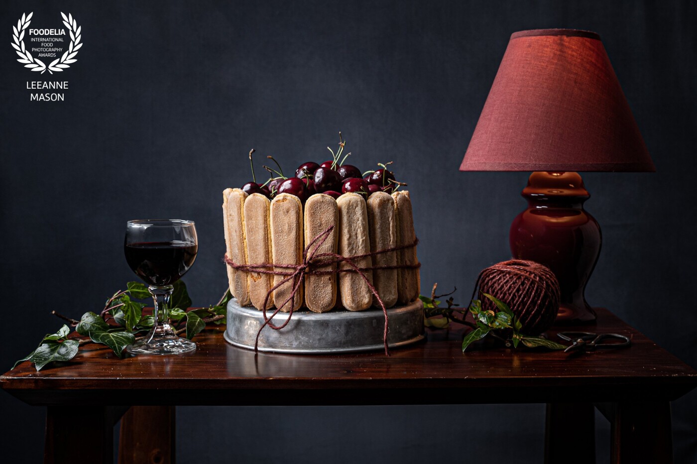 This is a Cherry Sponge decorated with Lady Fingers in a Still Life scene with a holiday theme colour composition.  I lit the background in addition to the lamp and used a softbox to light the scene from different angles.
