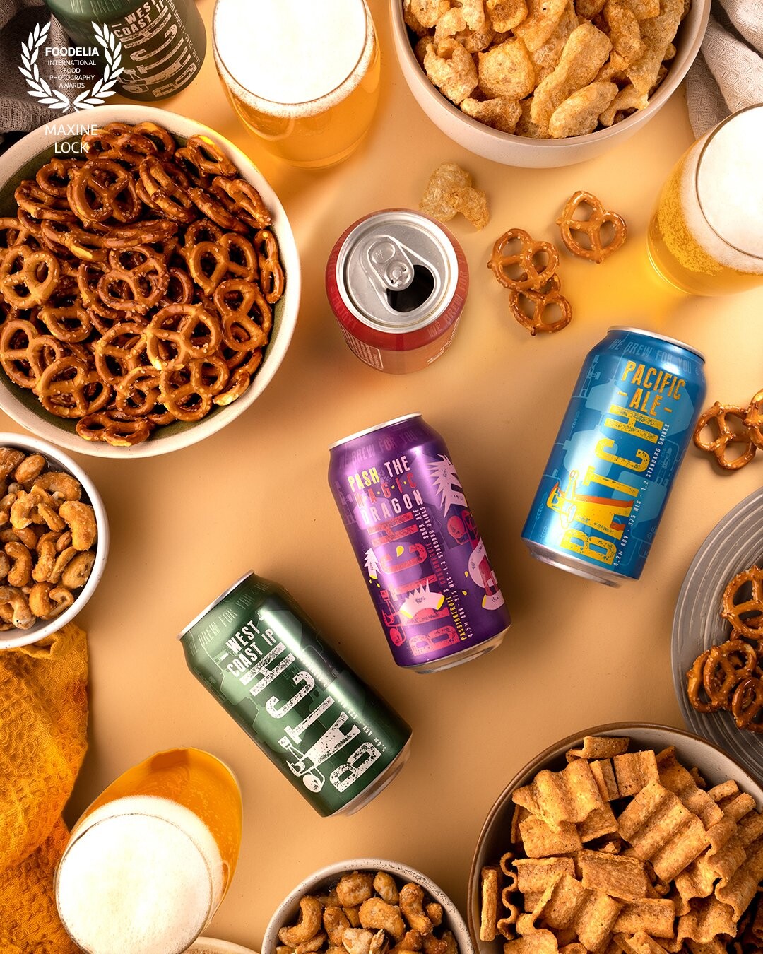 Beer photographed with both the cans itself, and the beer in glasses, with the image surrounded by nibbles that are usually served with beer.