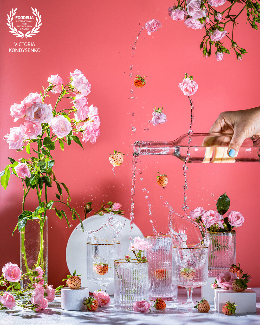 Different elegant glasses with sparkling wine, pink roses and strawberry, women hand is pouring wine