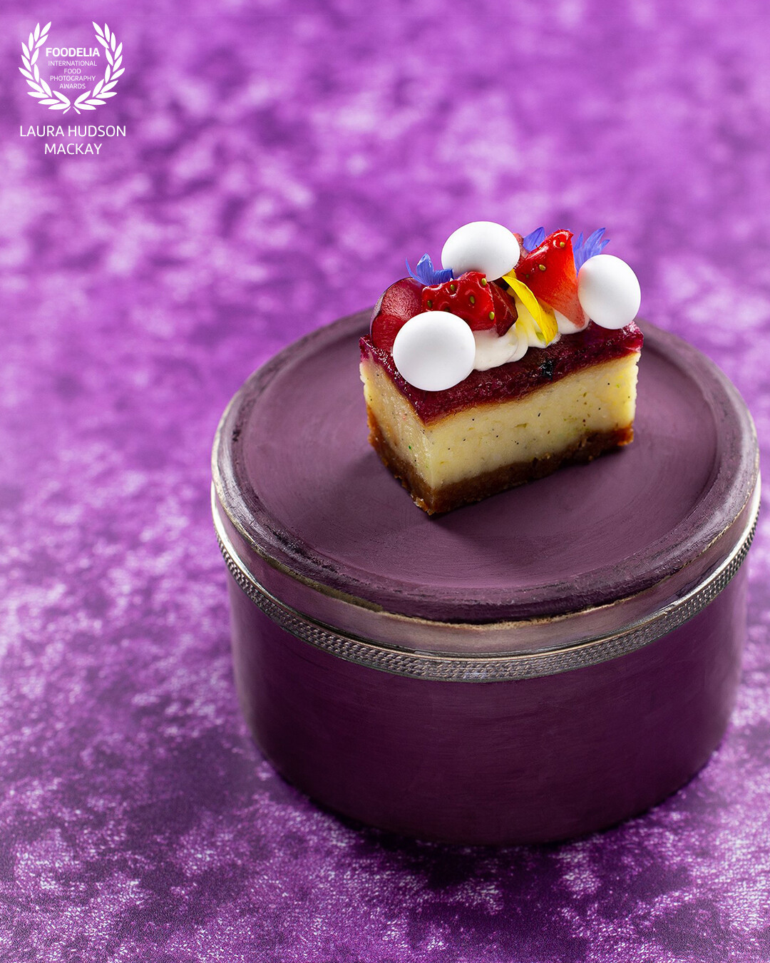 A perfect mixed berry cheesecake with raspberry and calendula.  Sitting on a purple stand, hand crafted from lime plaster, which serves as a pedestal for this small marvel. Collaboration with Scottish chef, Fraser Cameron. Together we combine artistry, flavour and vision.