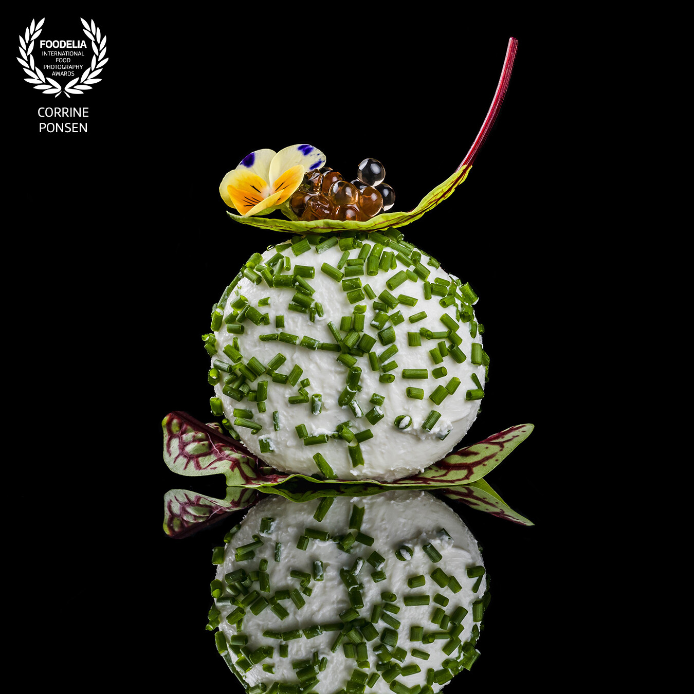 Creamy ball of goatcheese covered with chives and a eatable leaf and flower. On top some balsamico pearls.<br />
This is shot with a nikon Z8 and 105 mm with 2 flashes.