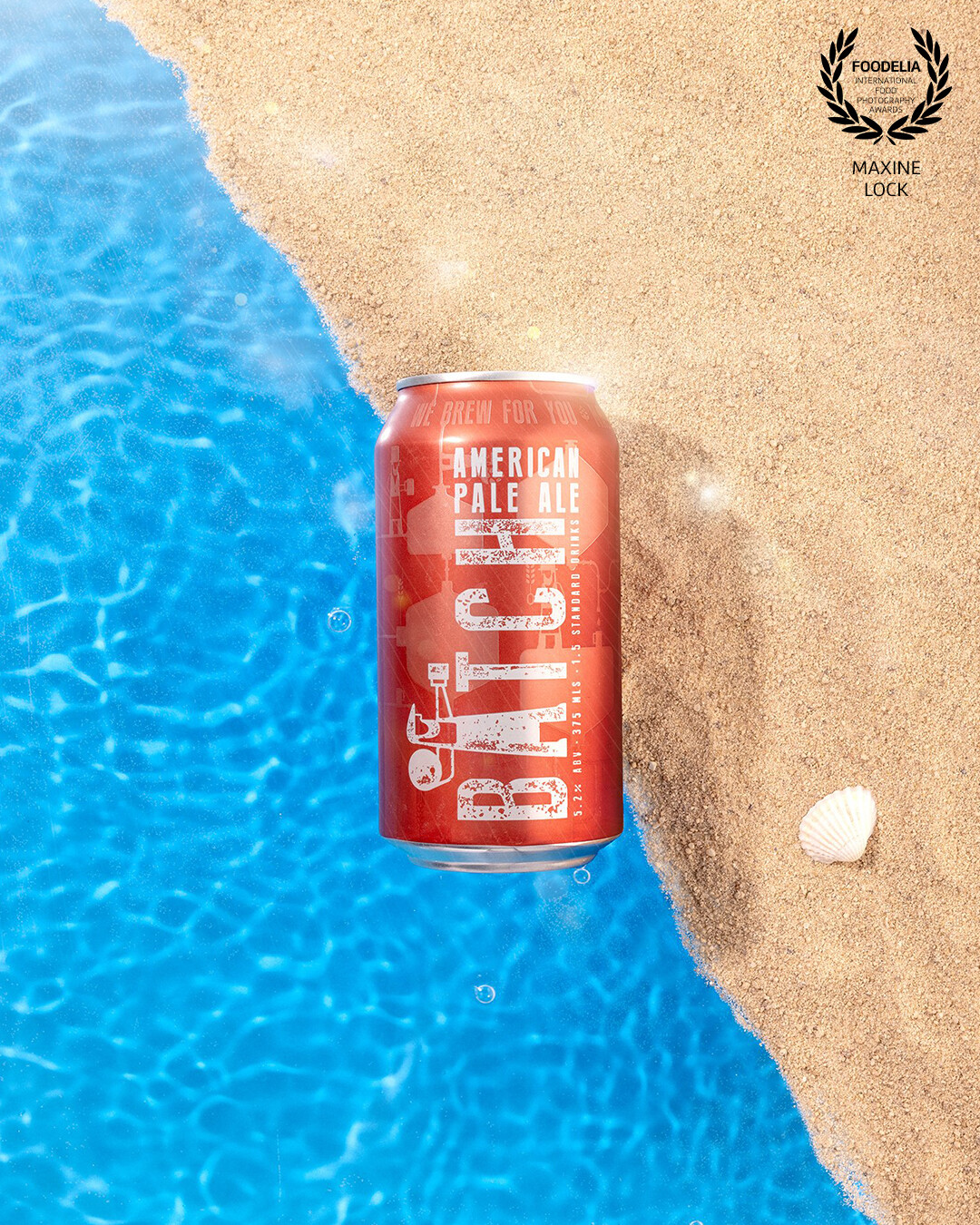 A beer can photographed with a beach scene creation as the backdrop. Sand, water and a blue backdrop were used to assemble a beach scene.