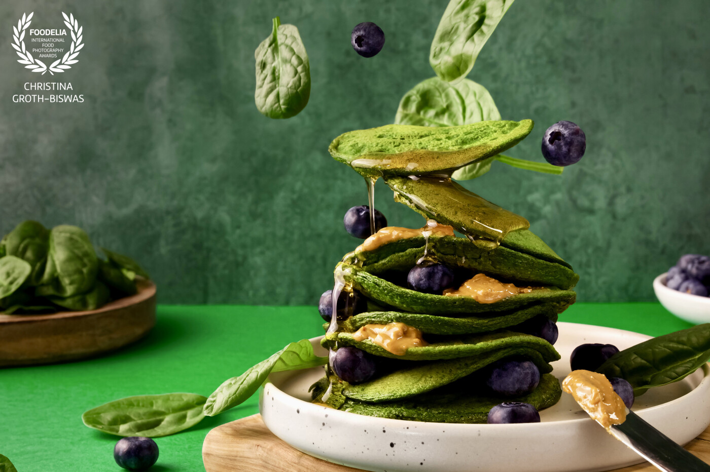 Levitation image of spinach pancakes topped with nut butter, berries and honey.