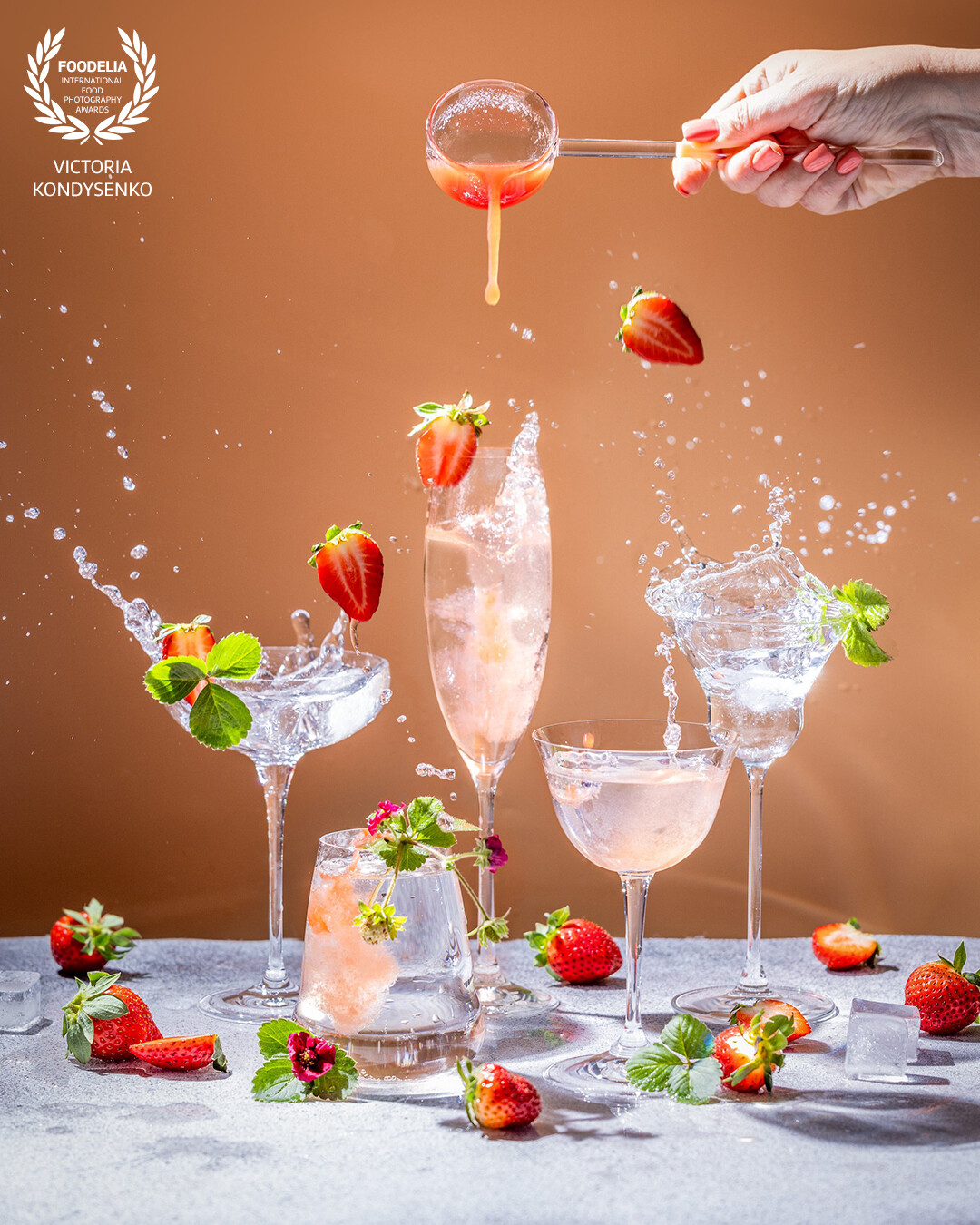 Different elegant glasses with sparkling wine and fresh strawberry, woman hand is pouring strawberry juice in glass.
