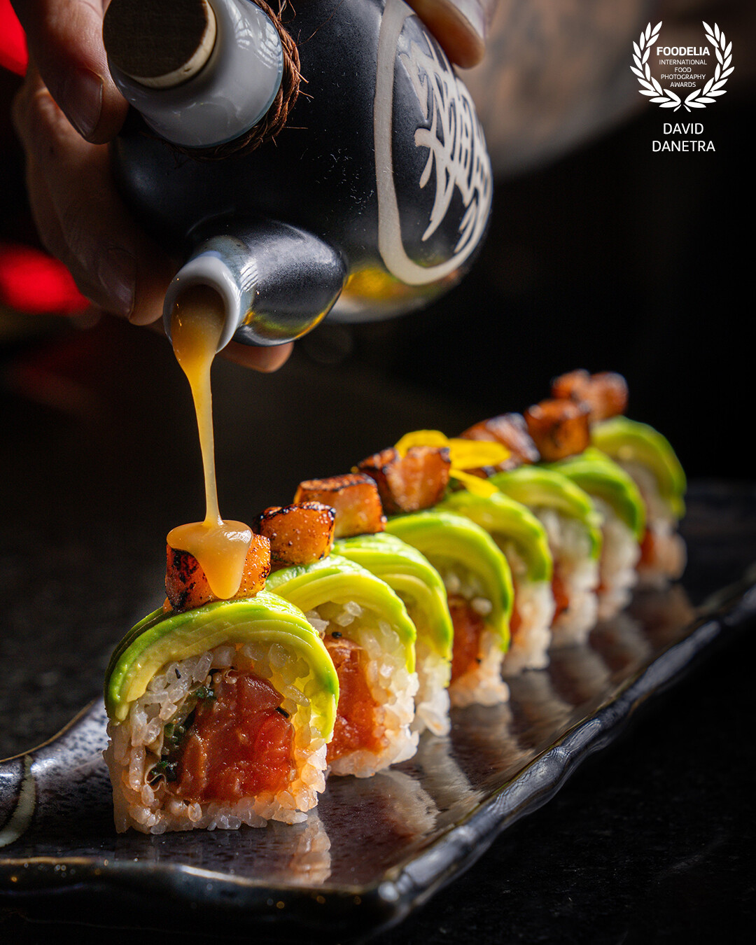 A close-up that highlights the texture and shine of the Maki Misoyaki from @kinjobog: Pacific Colombian tuna tartare wrapped in soy paper, layered with creamy avocado, and crowned with salmon glazed in miso sauce. The lighting and focus capture the freshness of each ingredient, showcasing the balance of colors and textures in this exquisite bite.