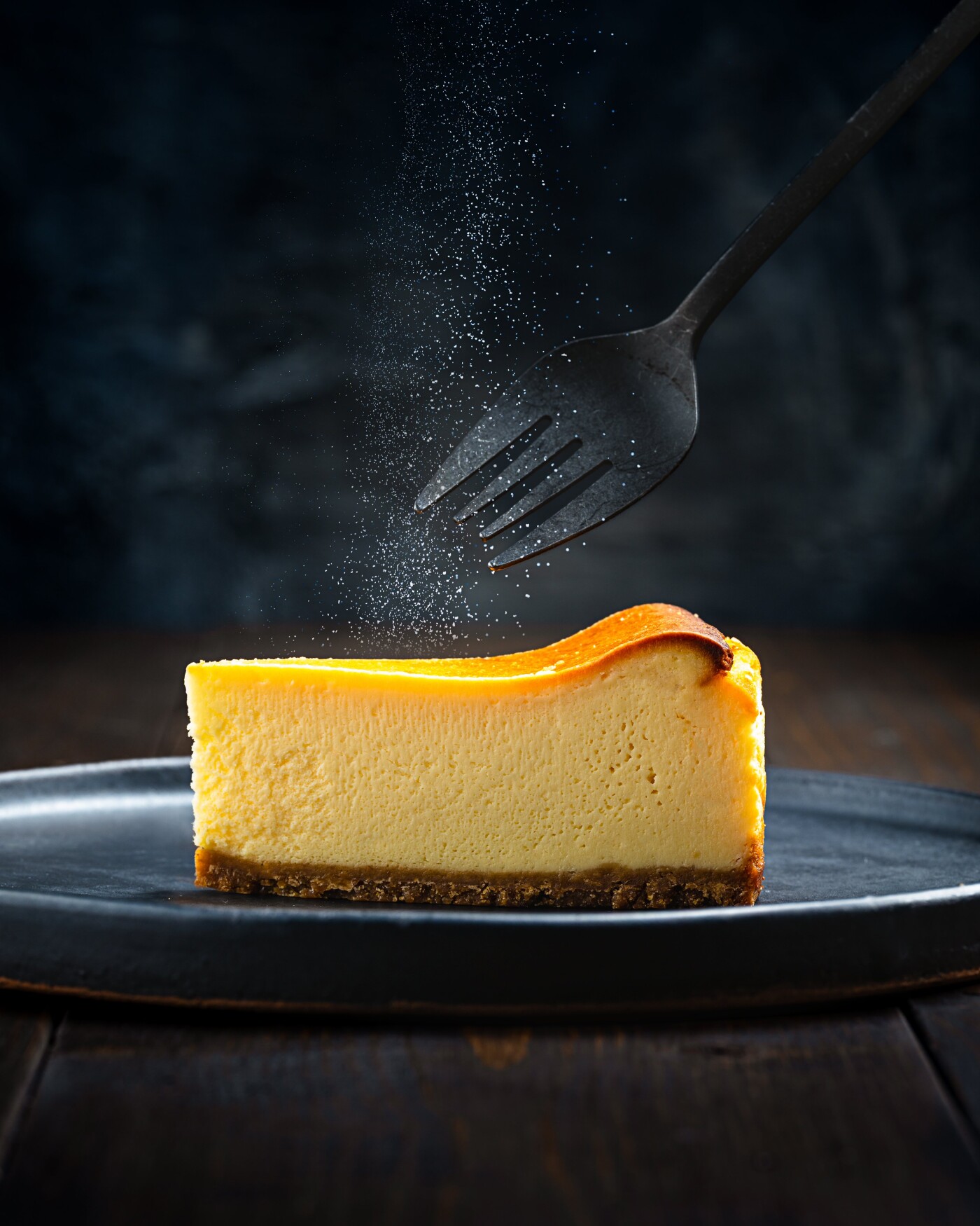 To capture the delicate texture of the cheesecake and the fine sprinkle of powdered sugar, a dark-to...