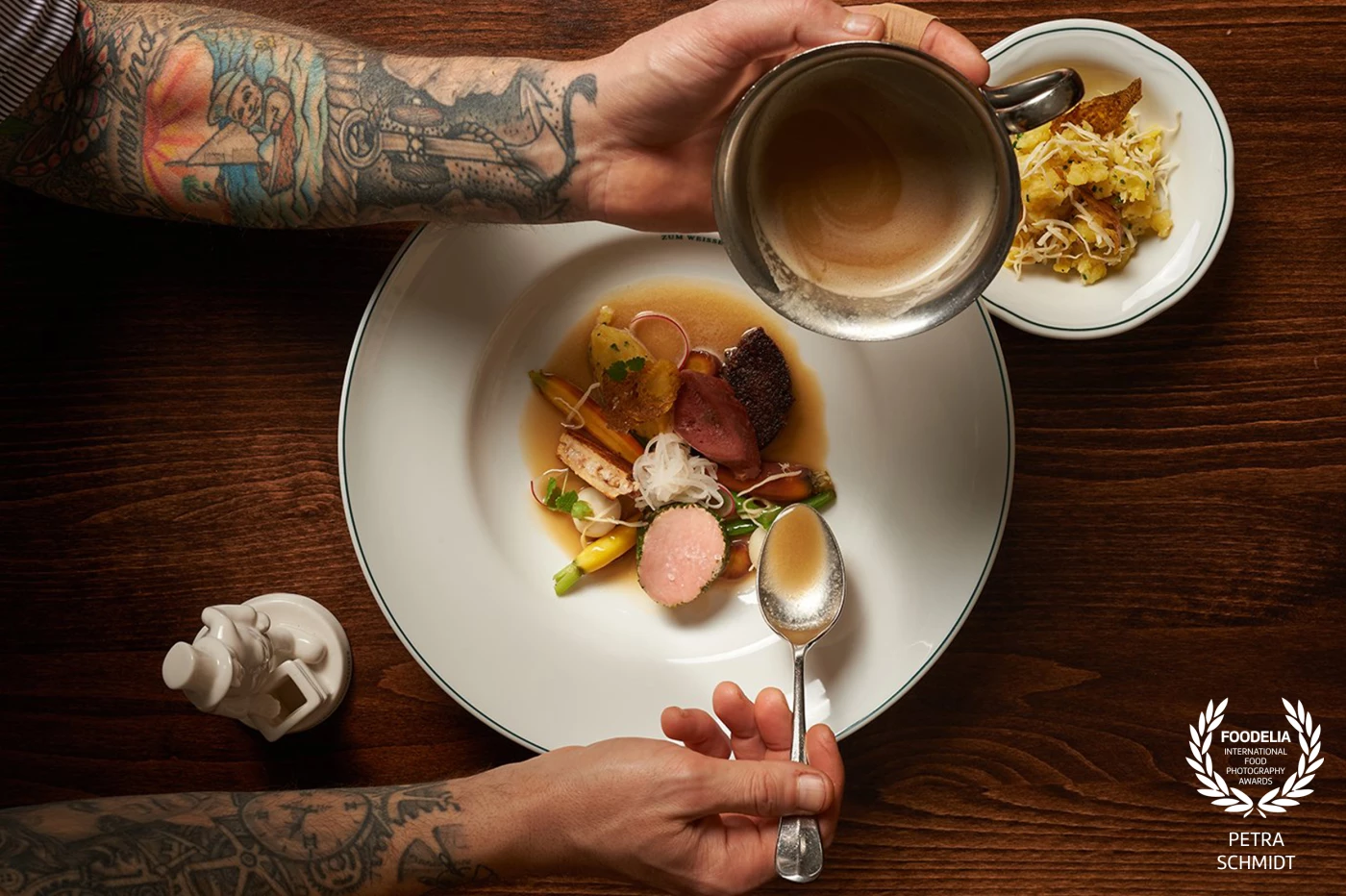 A masterpiece in the making. Chef Matthias, Head Chef of the iconic Zum Weißen Rauchfangkehrer, adds the final touch to his culinary creation. His tattooed hands, symbols of his journey and passion, reflect the artistry and precision he brings to each dish. Every detail is crafted with intention, every flavor balanced with care—a true representation of Viennese fine dining at its best.