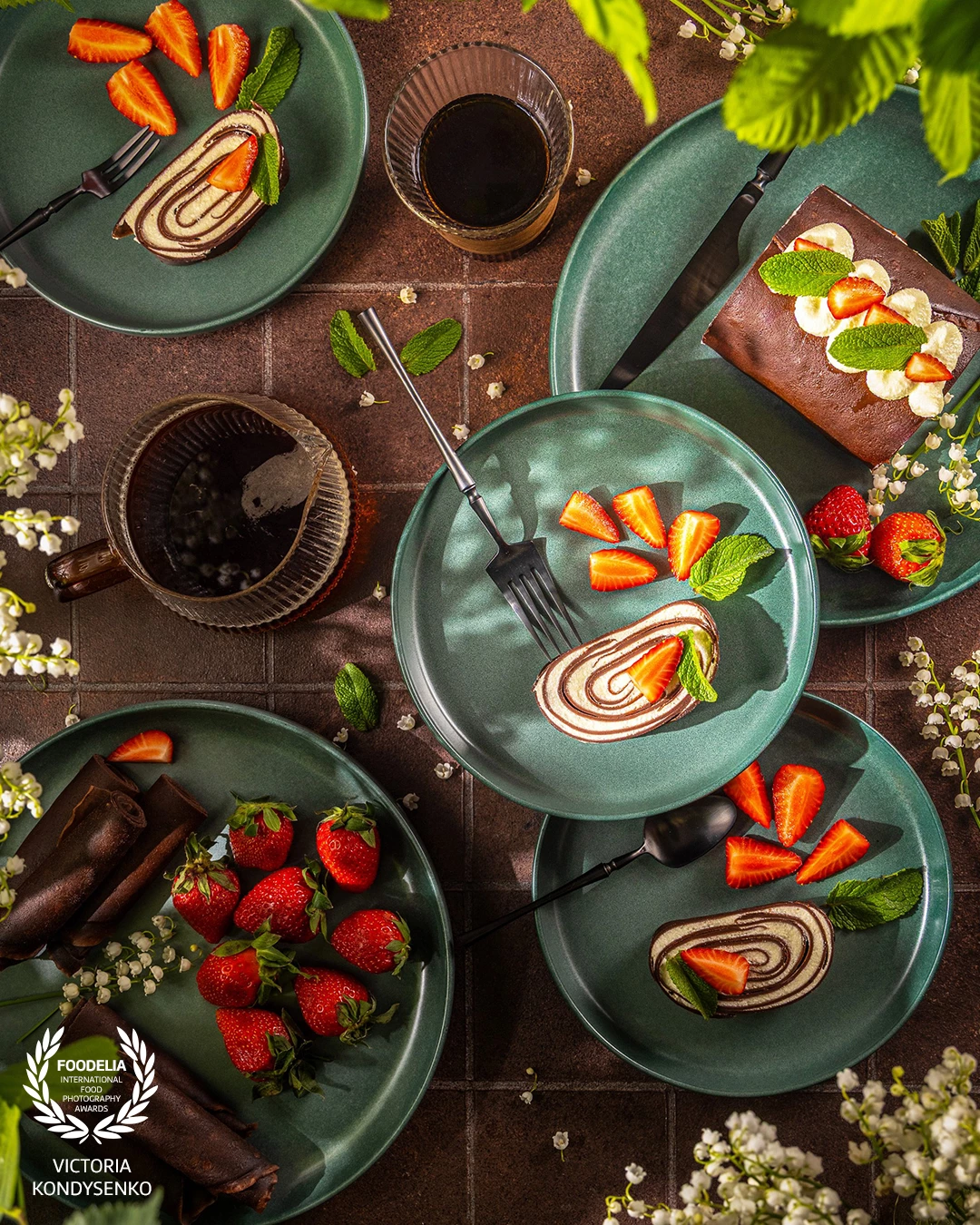 Pinwheel cake slices served on green plates with fresh strawberries and mint leaves, accompanied by cups of coffee, creating a delightful dessert setting.