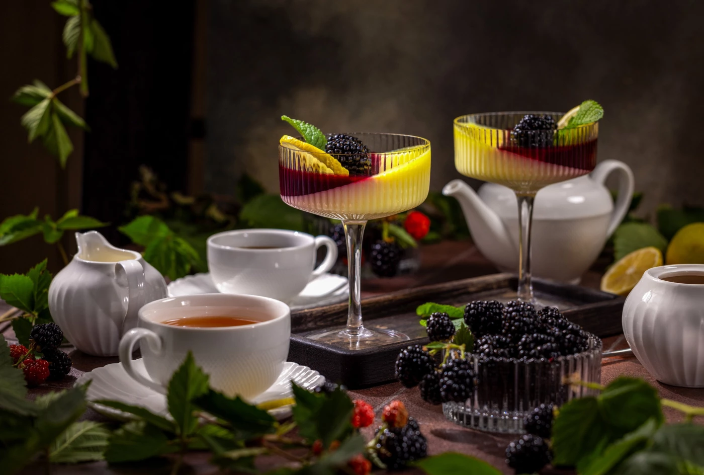 Two elegant glasses of panna cotta, topped with fresh blackberries, lemon slices, and mint leaves, c...