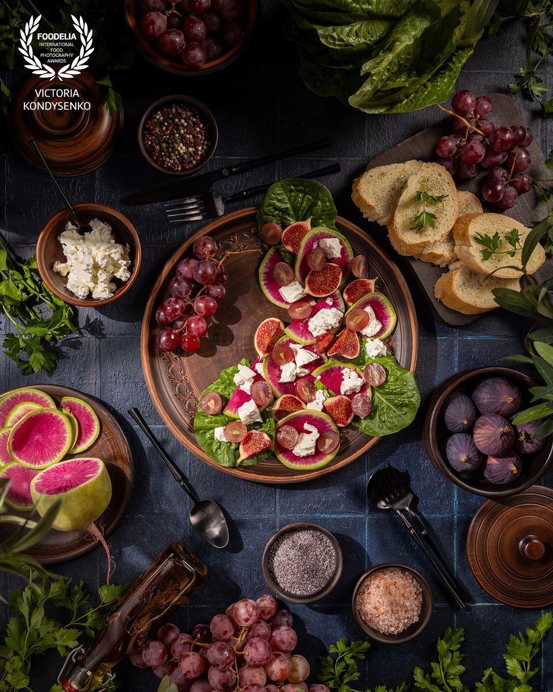 Healthy fresh salad with fruits and feta cheese. Table setting with vibrant salad of watermelon radishes, figs, grapes and feta, surrounded by bread, herbs and seasonings for a rustic, nutritious meal presentation