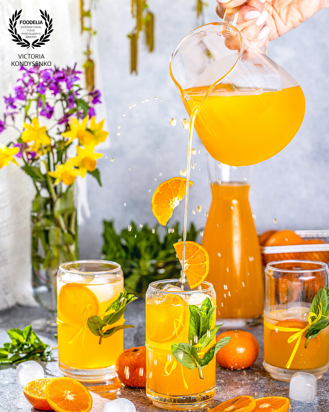 Glasses of tasty cocktail with tangerine and ice with splash, ingredients falling to glassfull. Delicious cooling drink for a warm spring noon.