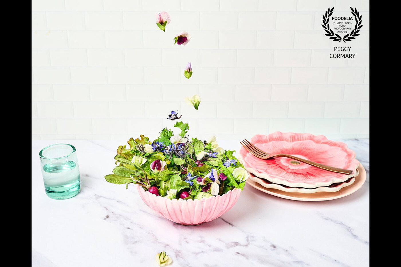 Bowl of green mixed salad placed on a white background to emphasize the edible flowers drop's colors and texture to a overall of freshness feel.
